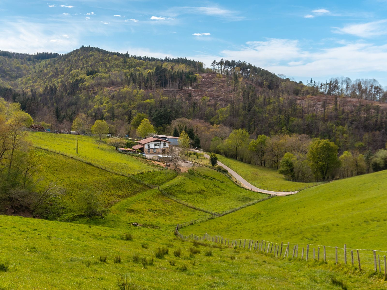Scenic Countryside Landscape with a House and Rolling Hills A picturesque view of a house nestled in a lush green valley surrounded by hills under a bright blue sky.