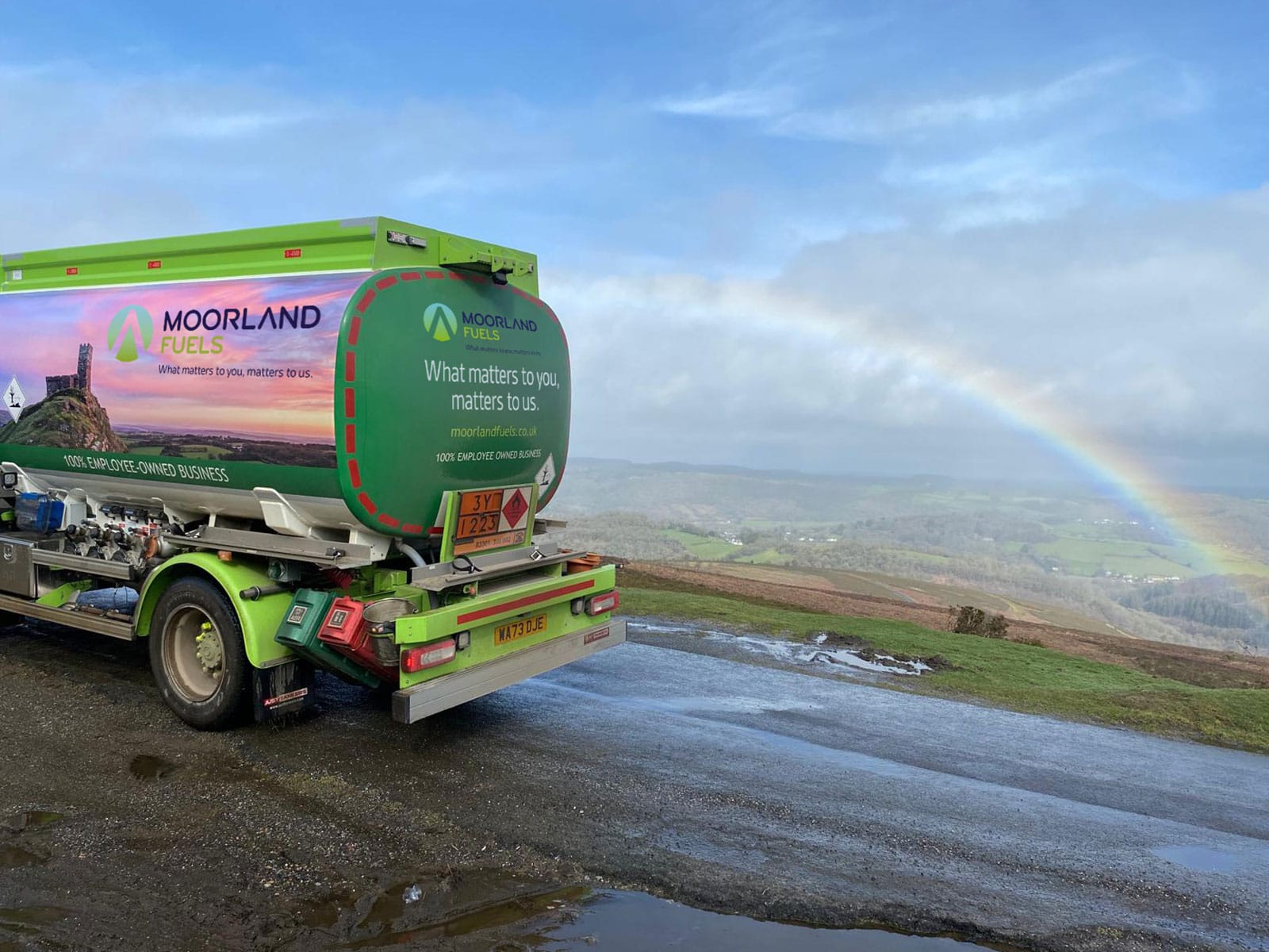 Moorland Truck with Rainbow Background A green truck from Moorland with a scenic view of a rainbow over the hills.