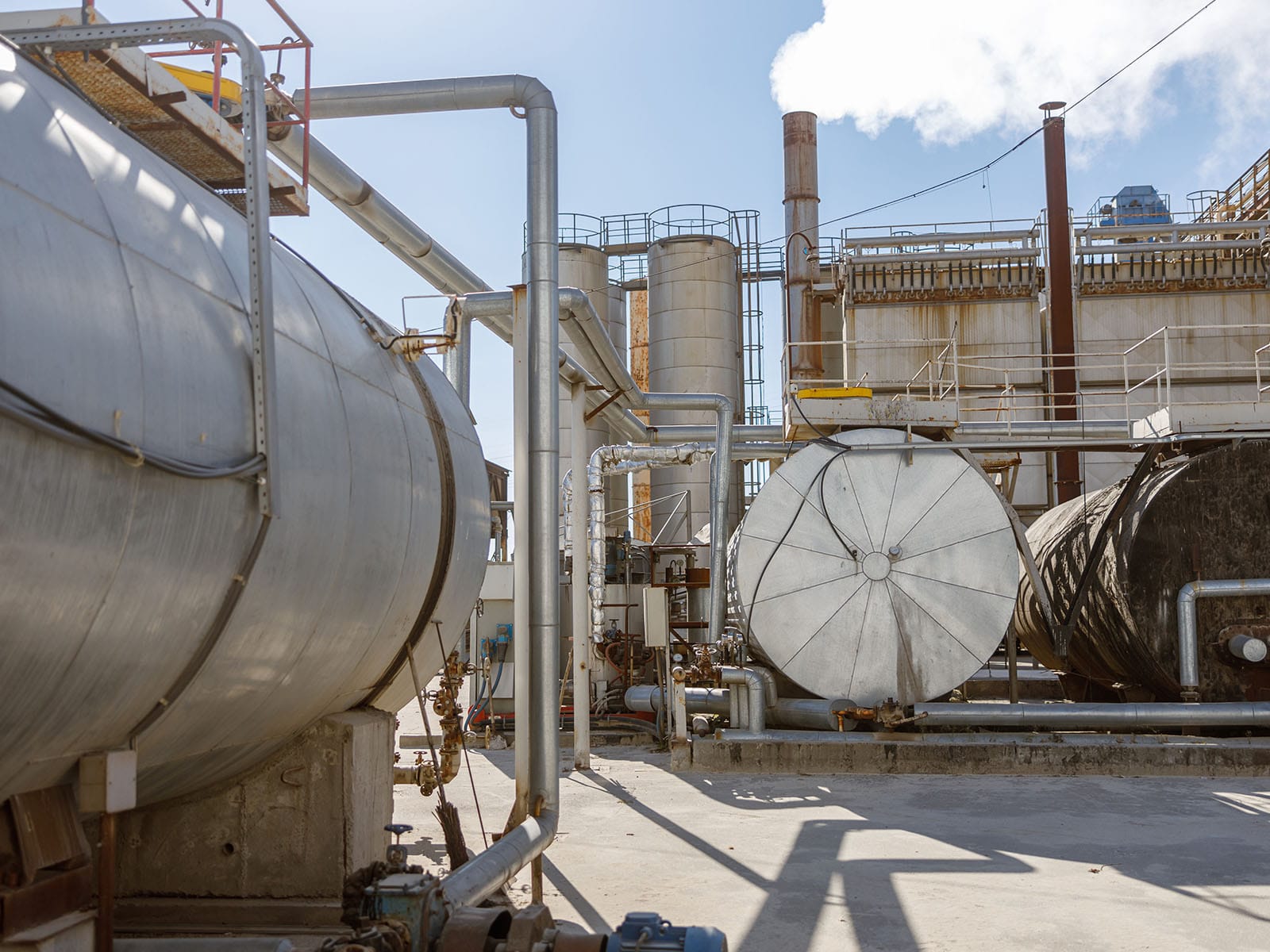 Industrial Equipment and Pipes in a Manufacturing Facility A view of large industrial tanks and pipes at a manufacturing plant under a clear blue sky.